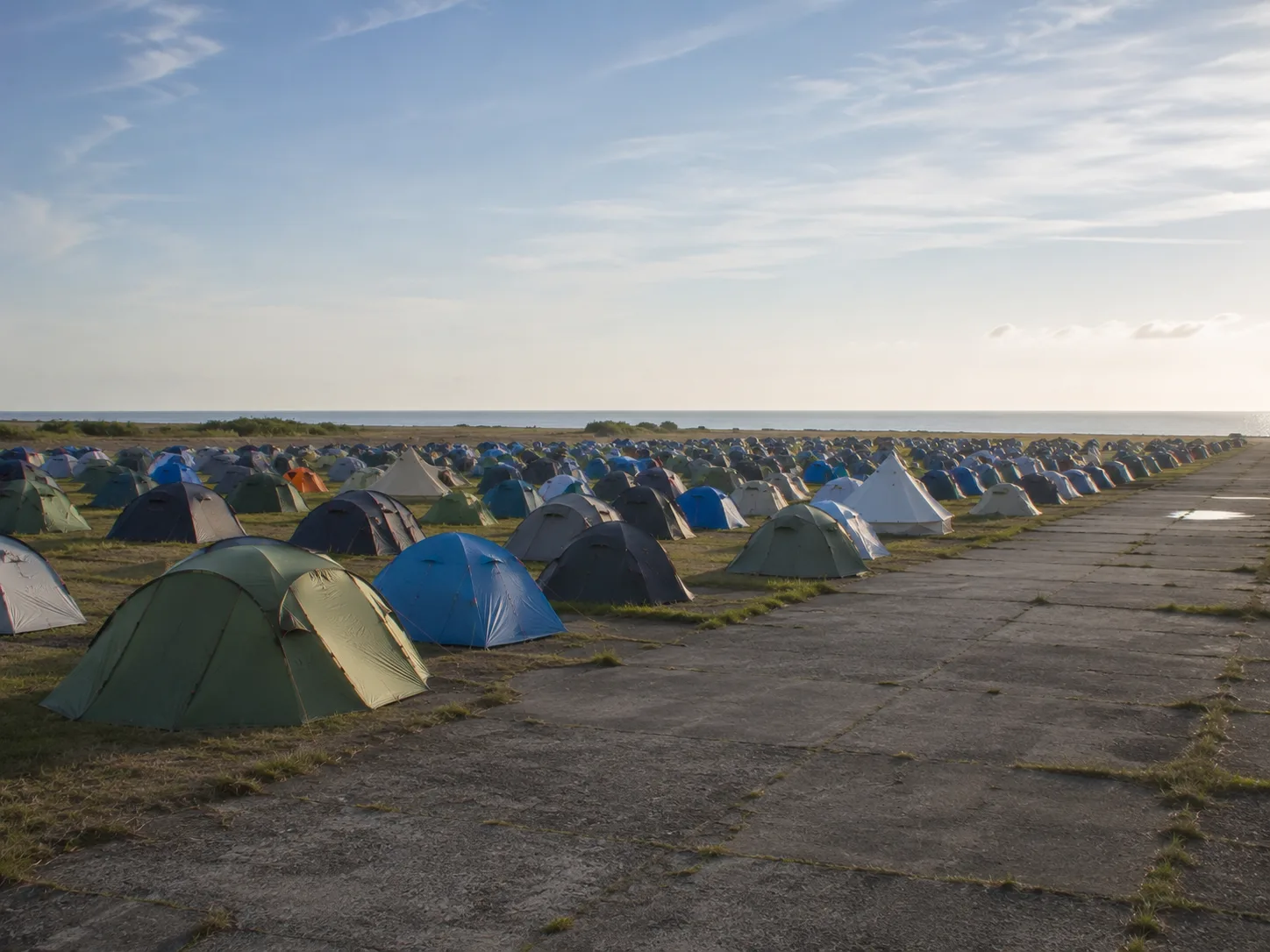 Kampeerterrein naast een breed betonnen platform, tenten op kort gras tot de horizon, daarachter de Oostzee onder een heldere koele hemel